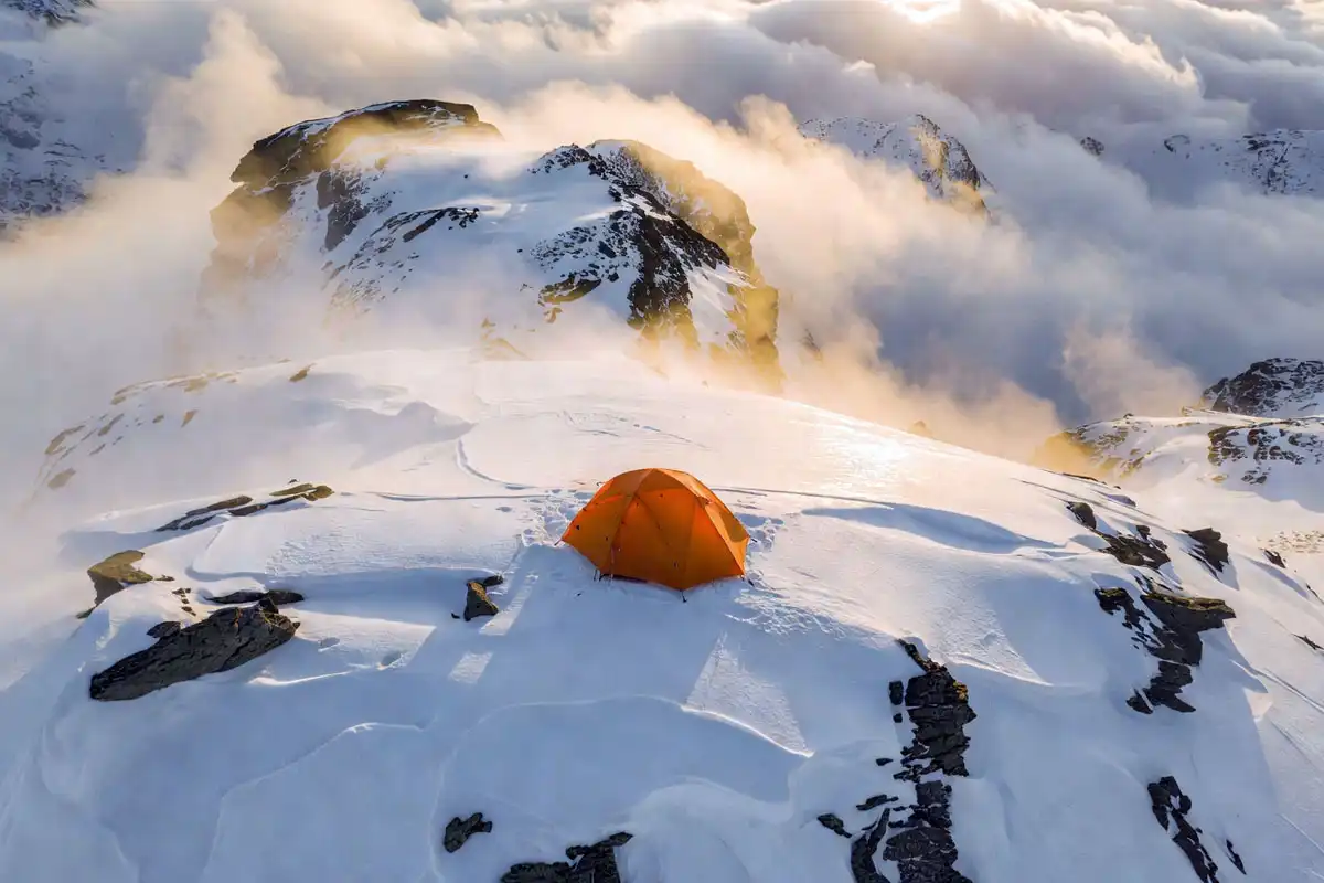 Bright orange tent visible on a snowy alpine ridge in fog