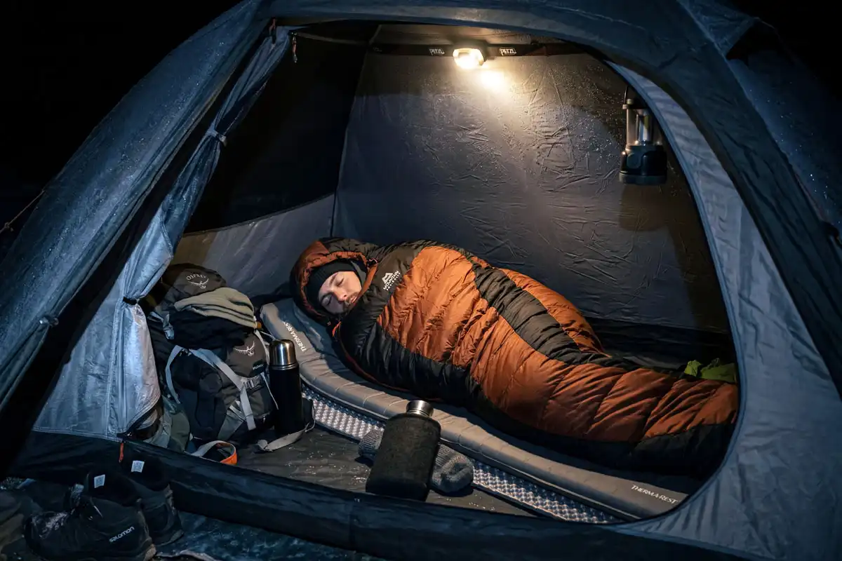 Camper tightening sleeping bag hood inside tent on freezing night
