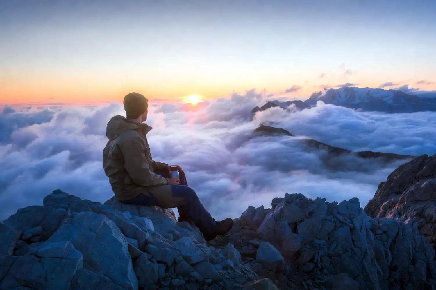 Hiker sitting on a rocky alpine ridge above clouds during a high altitude trek at sunrise