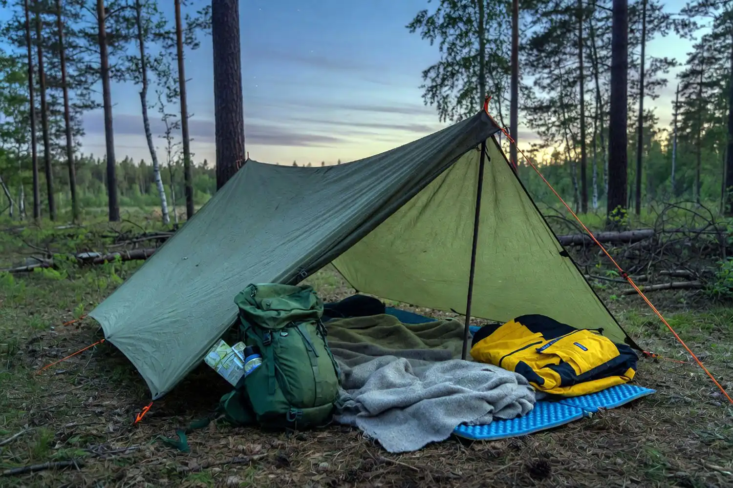 Low pitched A frame tarp with foam pad and wool blanket inside at dusk in a quiet forest clearing