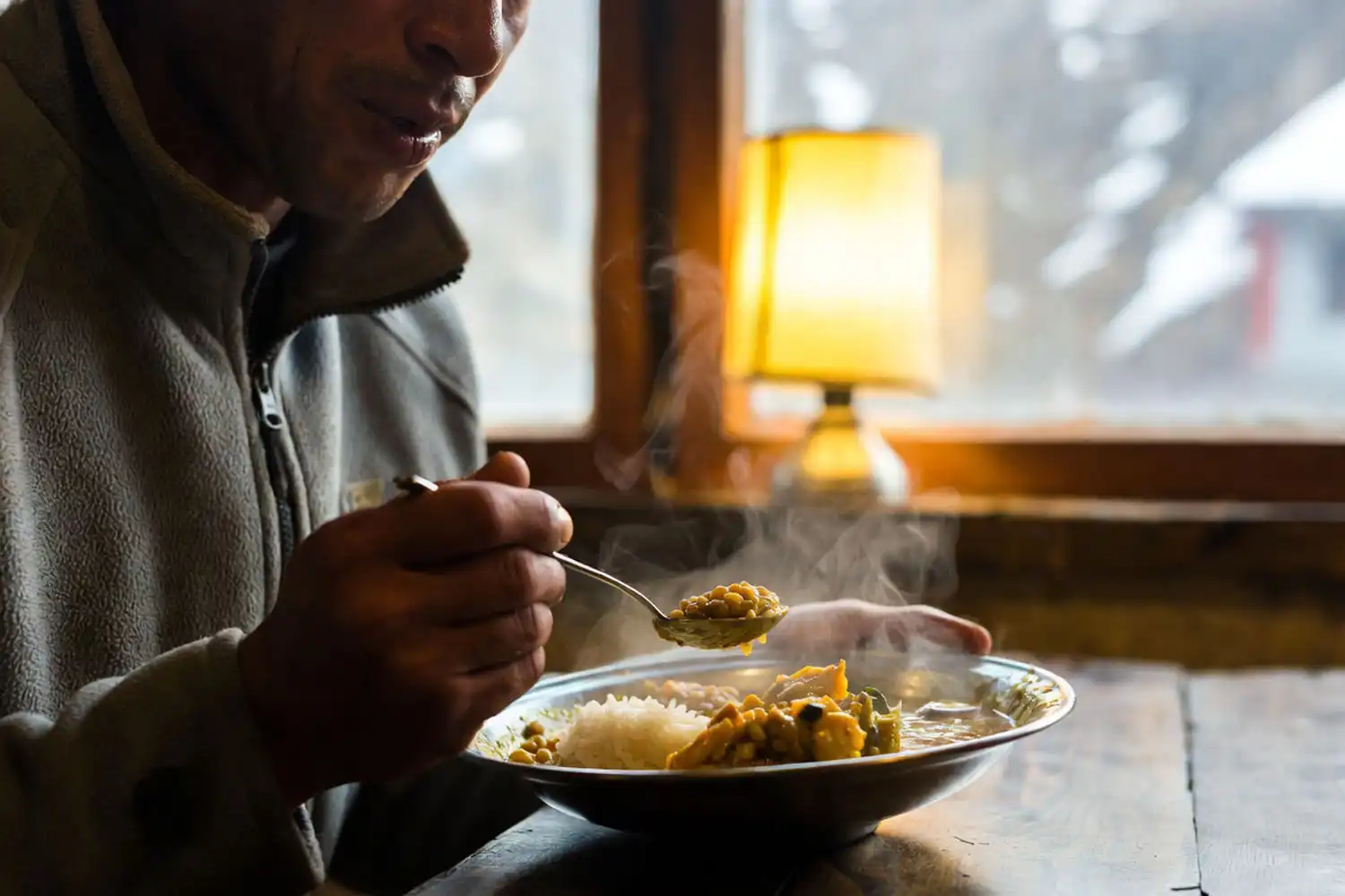 Solo trekker enjoying a hot plate of dal bhat at a wooden table inside a teahouse in the Khumbu region